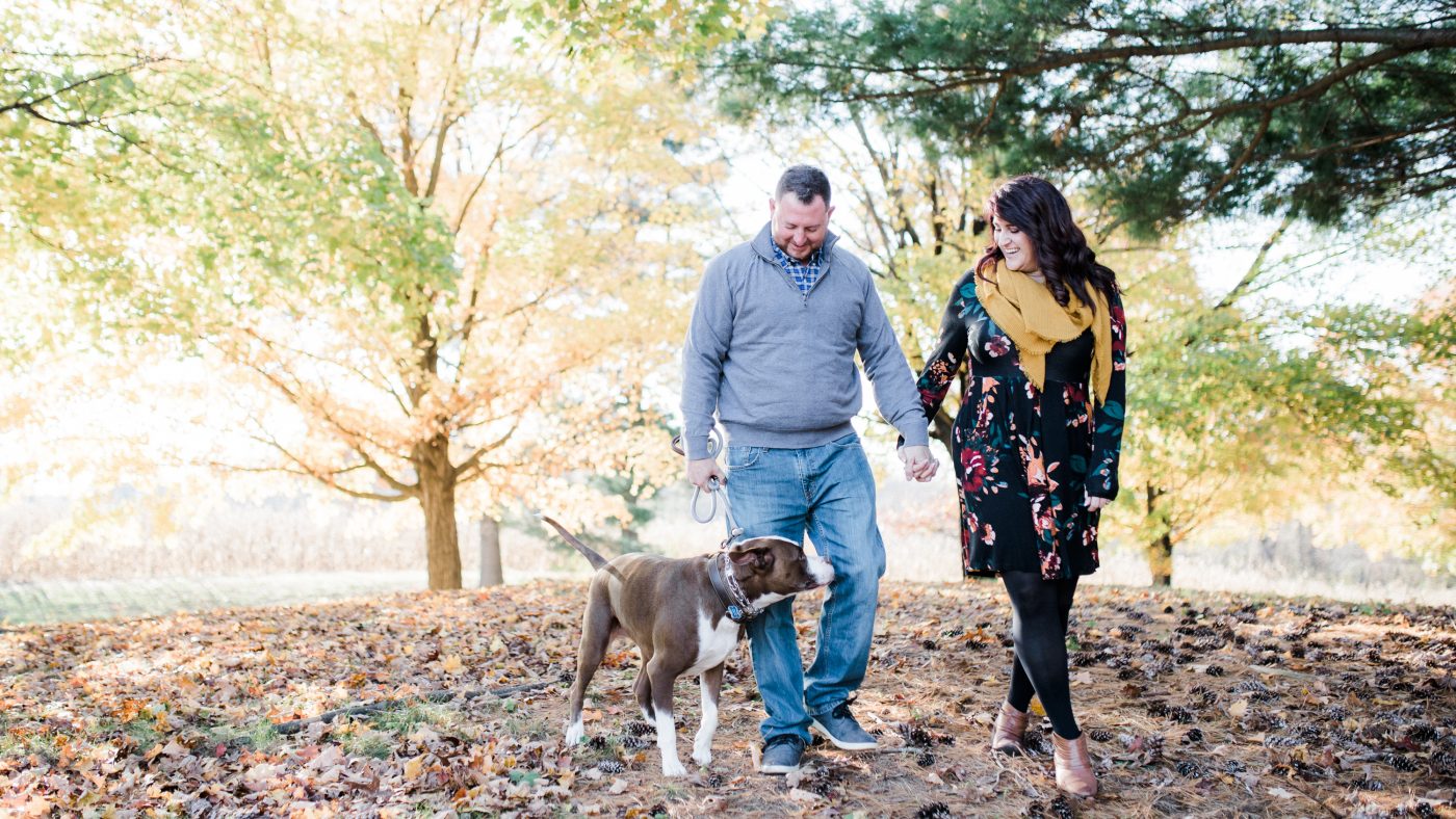 Couple walking with their dog under the colorful trees on their engagement session