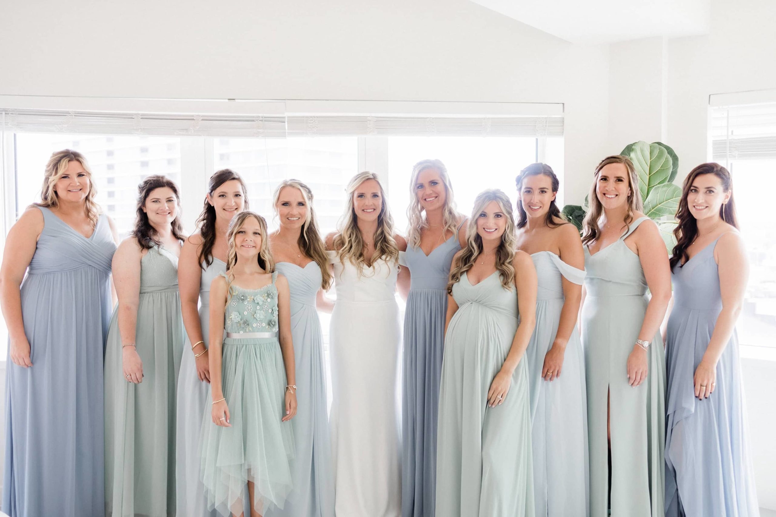 Bride and bridesmaids in blue, teal and green dresses by a window at the asbury hotel.