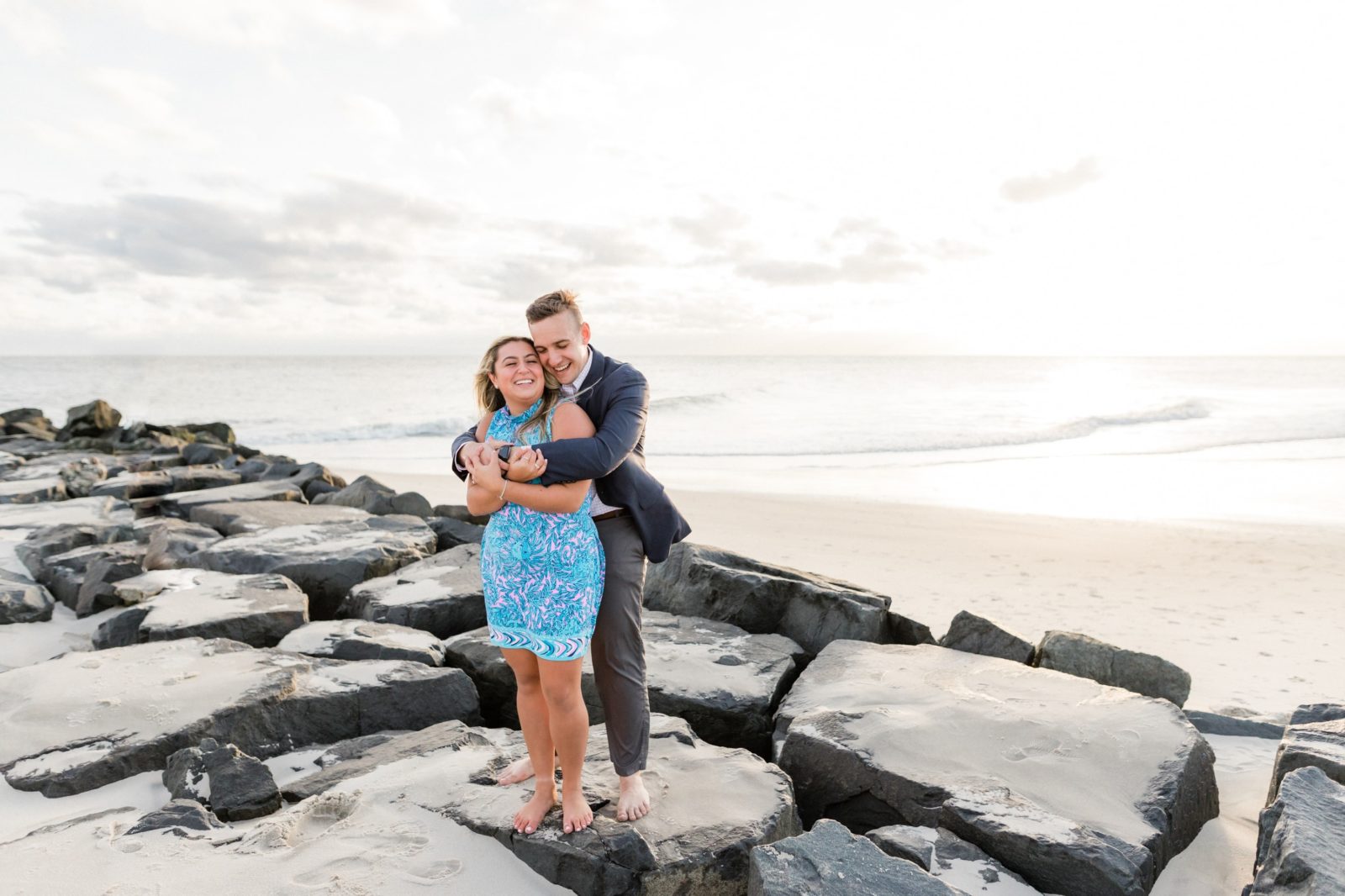 Photos of couple hugging and laughing by the rocks on the beach in Cape May 