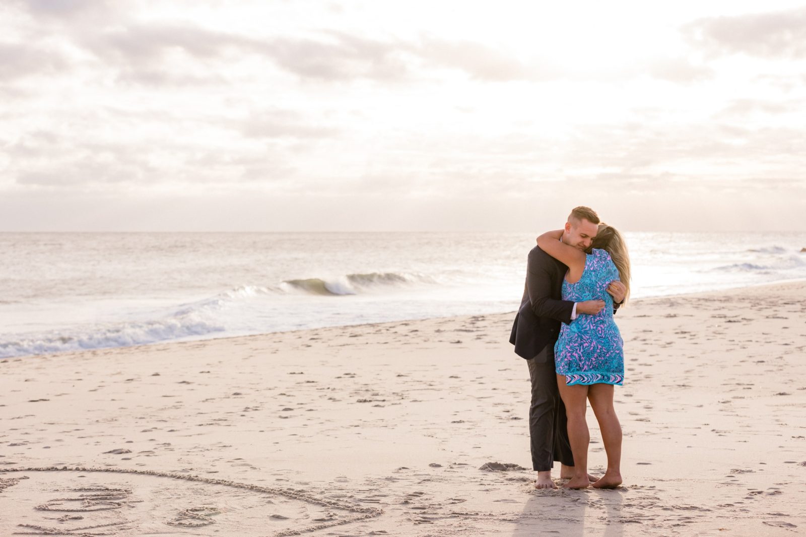 Couple hugging with the sun setting behind them during beach proposal in Cape May