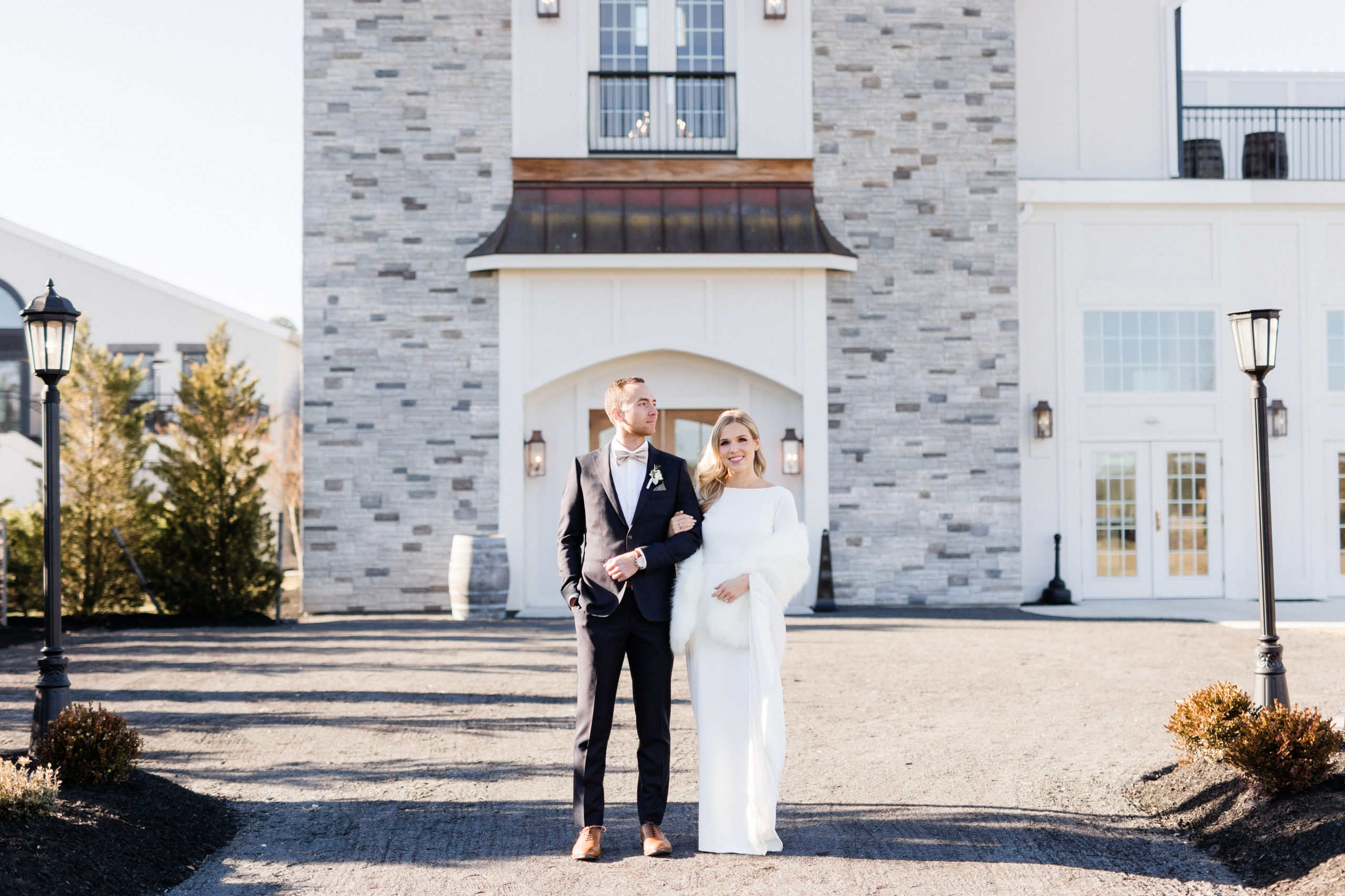 Bride and groom standing outside one of the ballrooms at the Renault Winery, with bride wearing faux fur shawl and a long sleeve dress and groom wearing a dark blue suit